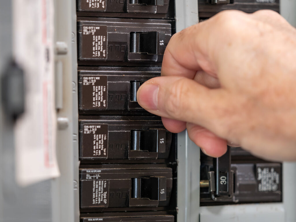 an electrician flipping a breaker switch on an electrical panel